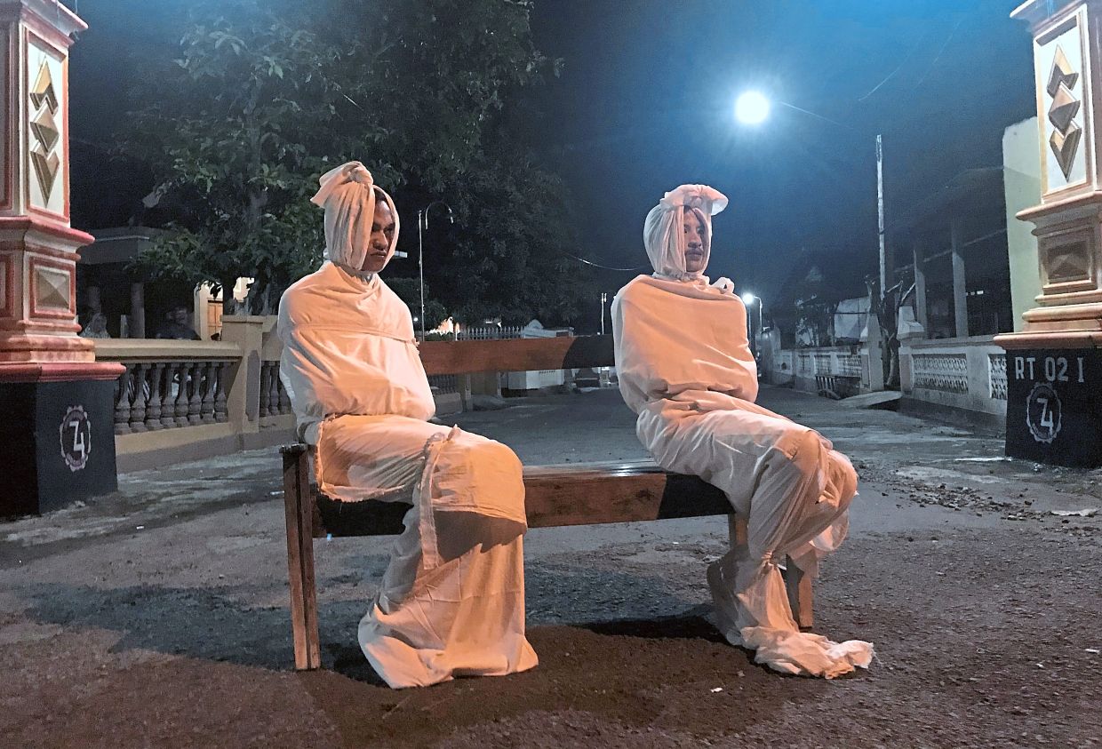  Two people wrapped in white cloth are sitting on a bench in the dark.